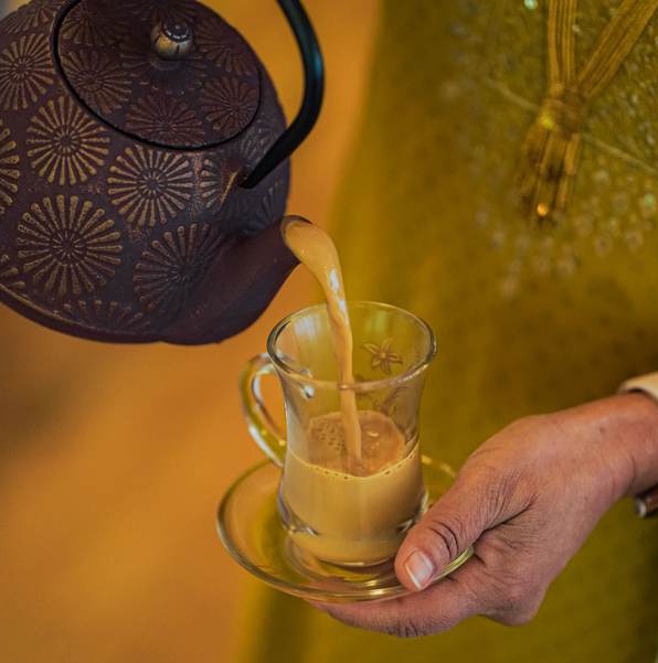 A woman in colorful traditional clothing pours a cup of tea